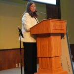 Secretary Kathy Blumenfeld of the Department of Administration stands at the podium and addresses the crowd